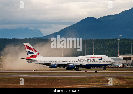 The jet engine thrust from a British Airways Boeing 747 kicks up a small dust storm as it taxies along the tarmac. Stock Photo