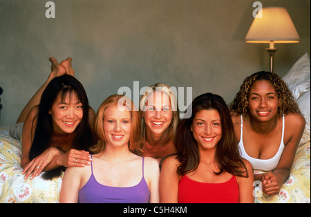 Colorful ethnic mixture of five female friends smiling at camera at home on bed Stock Photo