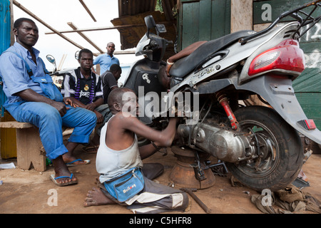 Disabled man repairing a moped engine outside a roadside workshop in Accra, Ghana. Stock Photo