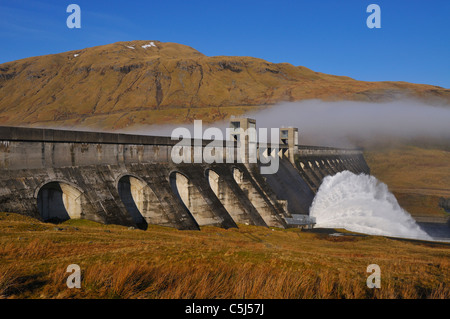 Glen Lyon HydroElectric dam venting water with a background of misty hills and blue sky, Perthshire, Scotland, UK. Stock Photo