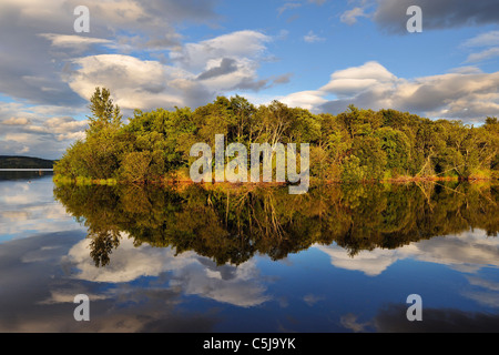 Dramatic evening light on a tree-covered island reflected in still water at Loch Tay, Perthshire, Scotland, UK Stock Photo