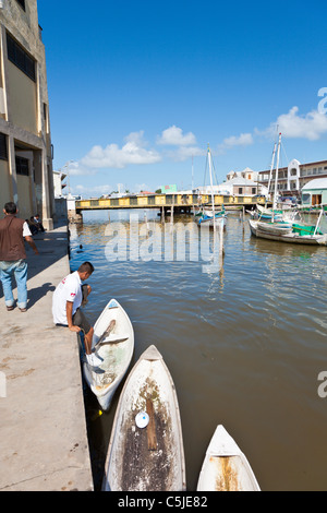 Man entering canoe type boat on Haulover Creek near swing bridge in Belize City, Belize Stock Photo