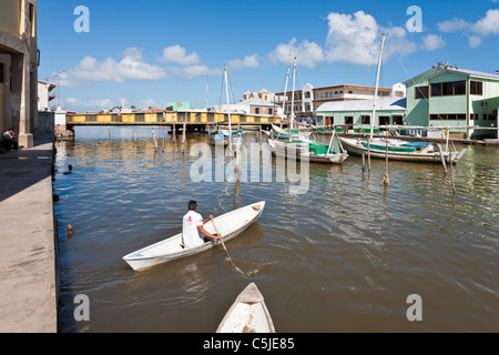 Man rowing canoe type boat on Haulover Creek near swing bridge in Belize City, Belize Stock Photo