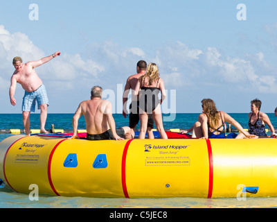 Young men and women jump on Island Hopper water trampoline off the coast of Bannister Island in the Caribbean Stock Photo