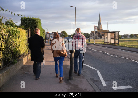 Two Millennial men and one woman walking down a street into the village in the evening seen from behind. Blackheath, London, England, UK Stock Photo