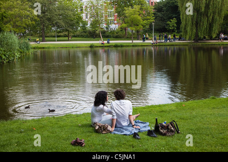 Young man and woman sitting on the grass, beside the lake in Vondelpark, Amsterdam Stock Photo