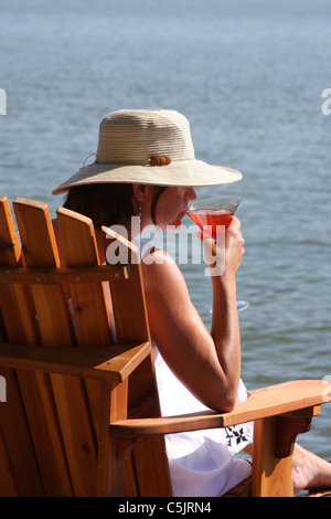 A lady sipping a cocktail next to a lake Stock Photo