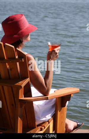 A lady drinking a cocktail next to a lake Stock Photo