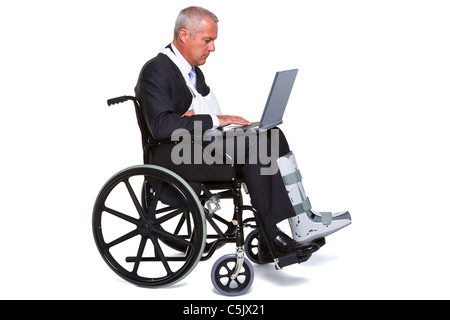 Photo of an injured businessman sitting in a wheelchair working on a laptop computer, isolated against a white background. Stock Photo