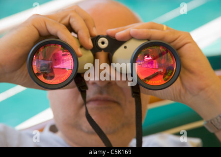 Bald man looking through binoculars with oink glasses, Bodrum, Gokova, Turkey Stock Photo