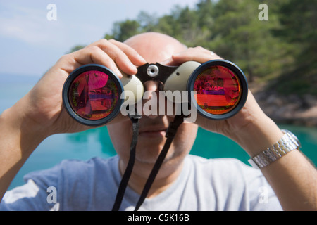 Bald man looking through binoculars with oink glasses, Bodrum, Gokova, Turkey Stock Photo