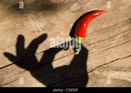 Male hand shadow cast over wooden table as if holding a red pepper Stock Photo