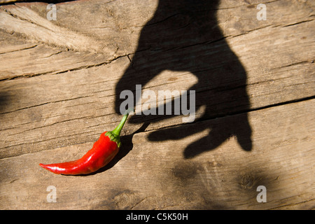 Male hand shadow cast over wooden table as if holding a red pepper Stock Photo