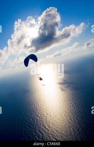 Powered paraglider flying over the sea with blue sky, clouds and shining sun Stock Photo