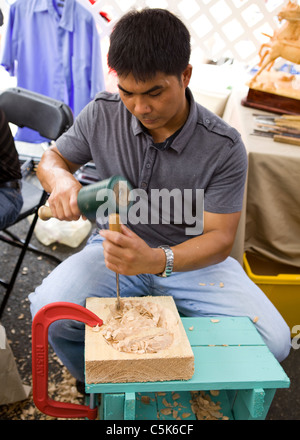 A Filipino man carving a piece of wood using chisel and rubber mallet Stock Photo
