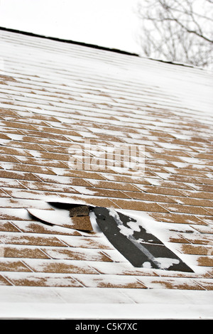 Damaged roof shingles blown off a home from a windy winter storm with strong winds. Stock Photo