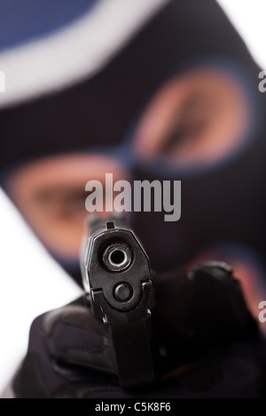 An angry looking man wearing a ski mask pointing a black handgun at the viewer. Shallow depth of field. Stock Photo