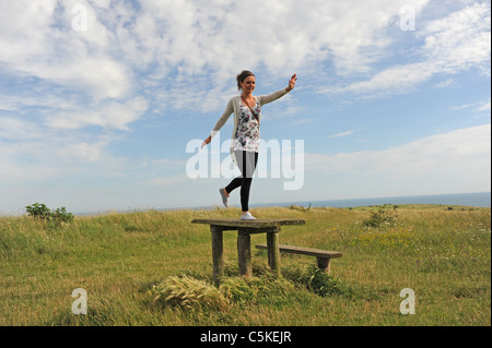 Young woman having fun leaping across a picnic table on Sheepcote Valley downs near Brighton Sussex UK Stock Photo