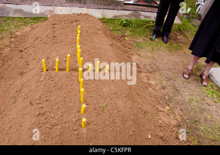 Cross formed from the candle on the newly stacked grave. Stock Photo