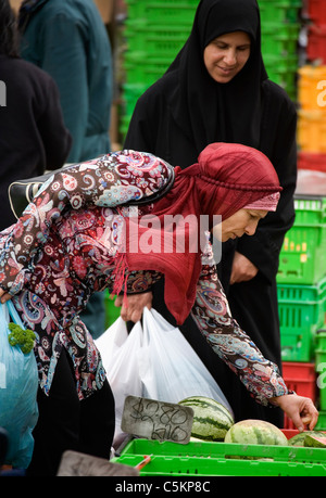 Two Muslim women, one wearing colourful dress, the other in black, at  outdoor fruit and vegetable market, Wellington, New Stock Photo