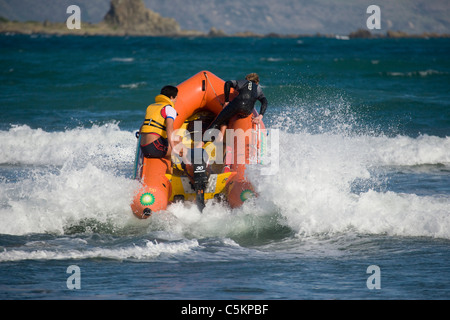 Inflatable surf rescue boat with outboard motor powering through breaking waves with two men onboard, Lyall Bay, Wellington, Stock Photo