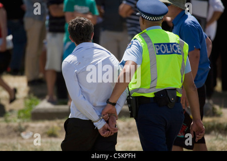 A young man, back view, being taken away in handcuffs by a policeman at Trentham Racecourse on Wellington Cup Day, Upper Hutt, Stock Photo