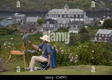 Monhegan Island, Maine -- Female artist paints using an easle atop a hillside overlooking Monhegan Island harbor and village, Stock Photo