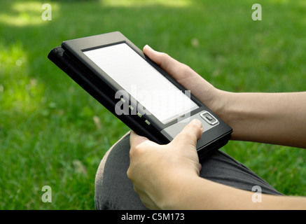 Young woman reads electronic book sitting on the grass. Shallow depth of field. Stock Photo