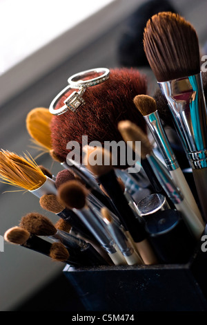 Two diamond wedding rings a band and engagement ring laying on top of some professional makeup brushes. Stock Photo