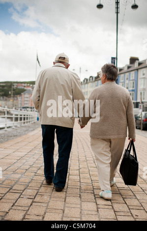 a senior elderly couple walking hand in hand on aberystwyth promenade wales uk Stock Photo