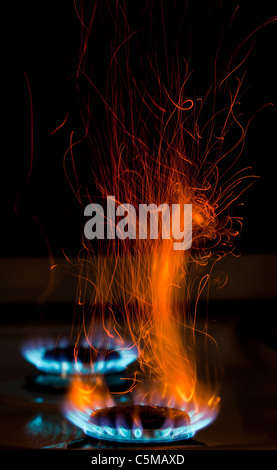 red and orange sparks and flames above gas stove burning with blue flames Stock Photo