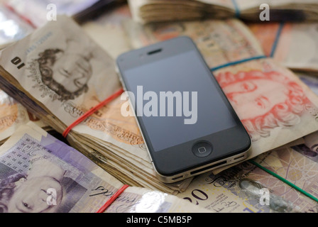 An Apple iPhone 4 with a blank screen lying on top of a very large number of British banknotes. Stock Photo