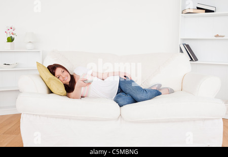 Attractive red-haired female watching tv while lying on a sofa Stock Photo