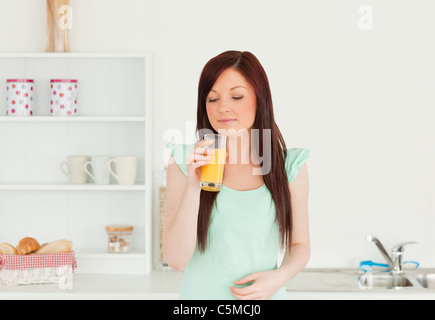 Attractive red-haired woman enjoying a glass of orange juice in the kitchen Stock Photo