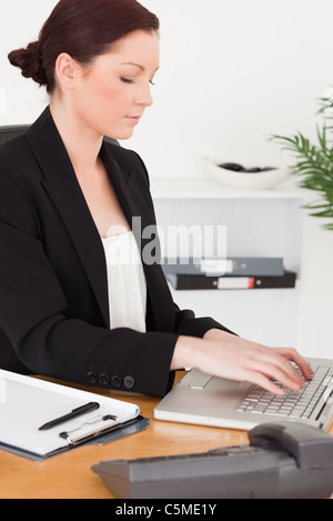Young attractive red-haired woman in suit typing on her laptop Stock Photo