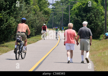 Elderly couple holding hands walking along a bike path in the summer on a sunny blue sky day. USA Stock Photo