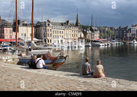 Couples sitting on the harbour wall at Honfleur, Normandy, France Stock Photo