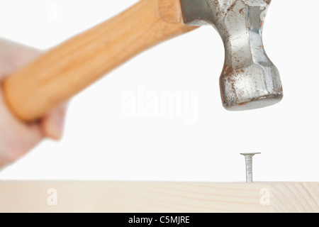 Hand holding a hammer to drive a nail into a wooden board Stock Photo