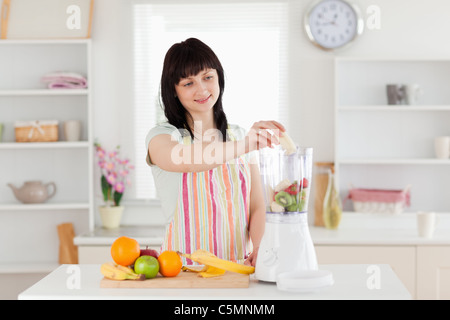 Gorgeous brunette woman putting vegetables in a mixer while standing Stock Photo