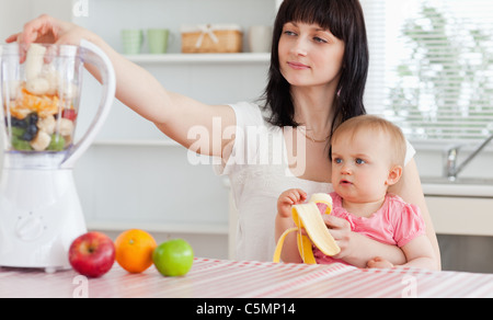 Gorgeous brunette woman putting vegetables in a mixer Stock Photo