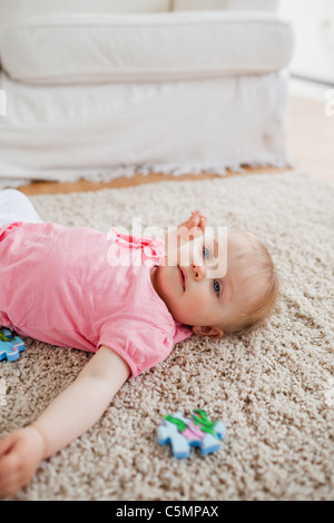 Lovely blond baby playing with puzzle pieces while lying on a carpet Stock Photo
