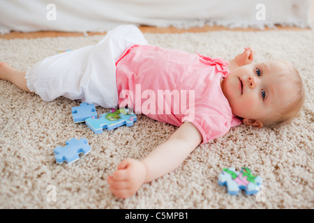Cute blond baby playing with puzzle pieces while lying on a carpet Stock Photo