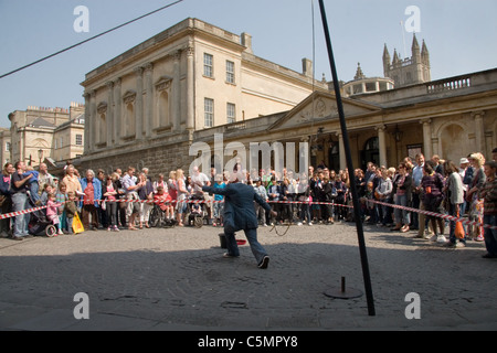 A crowd gathers to watch a street act outside the Roman Baths; Stall Street, Bath, Somerset, UK Stock Photo