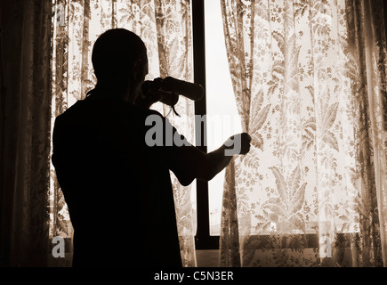Man with binoculars looking out of window from behind net curtain: nosey neighbour, spy, undercover cop, pervert, stalker... concept Stock Photo