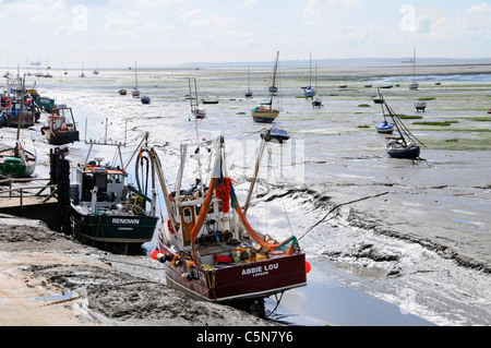 Cockle & shellfish fishing boats moored in Thames Estuary on mud flats low tide creek Old Leigh Essex coast Kent coastline & boats distant England UK Stock Photo