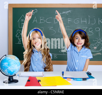 clever students in classroom raising hand with blackboard background Stock Photo