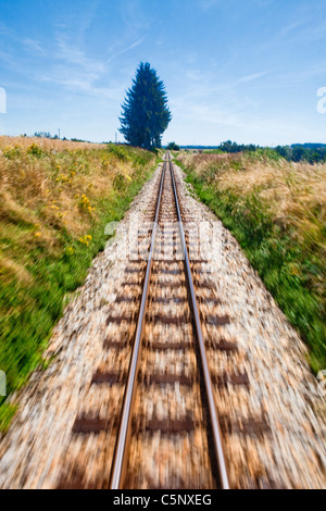 View of narrow gauge railroad track from rear window of train riding through landscape Stock Photo