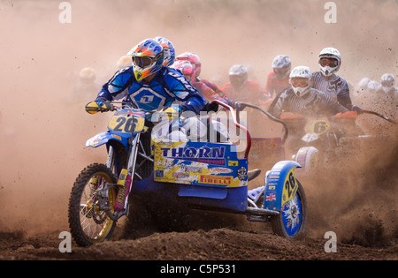 Riders racing through the dust at the start of a sidecar motocross race Stock Photo