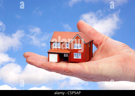 Photo of a hand holding a model house against a sky background. Stock Photo