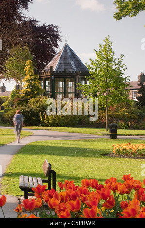 Beautiful landscaped village park, colourful flowerbeds, neat lawn, historic gazebo (Round House) & person - Grange Park Burley-in-Wharfedale, England Stock Photo